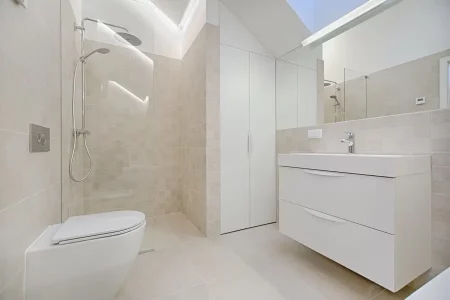 Salle de bain sur mesure par L. Cuisine et Aménagement, entièrement blanche équipée d'une douche, d'un placard, d'un meuble une vasque et d'un immense miroir, créant une ambiance lumineuse et épurée. Chaque élément est soigneusement intégré pour offrir un espace fonctionnel et esthétique.